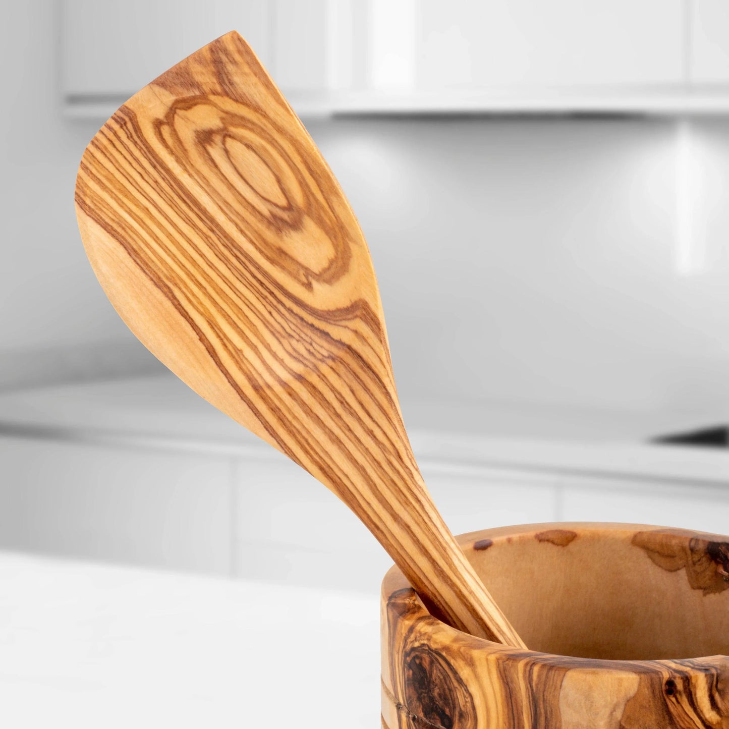 Handmade olive wood kitchen utensils spatula with natural wood grain pattern in a wooden bowl
