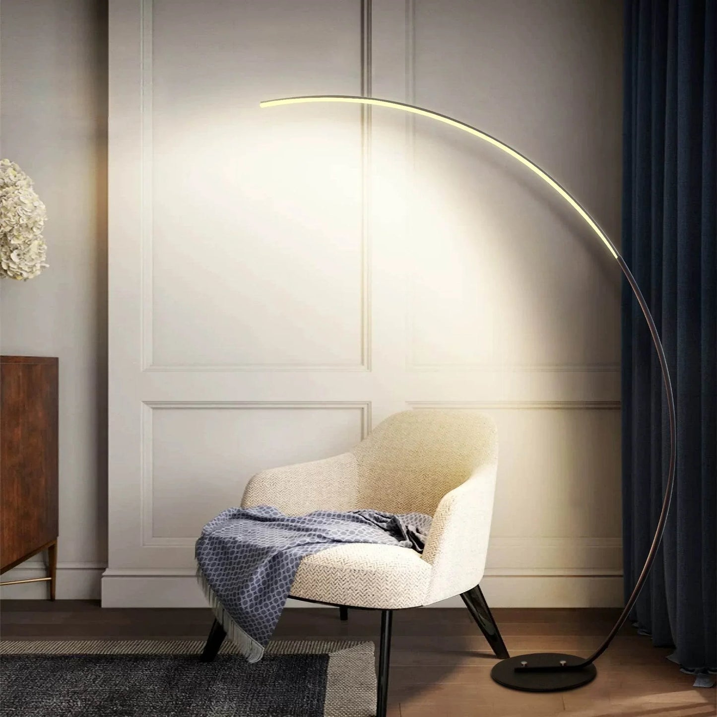 Sangria Apricot modern curve floor lamp illuminating beside beige chair with throw blanket in living room