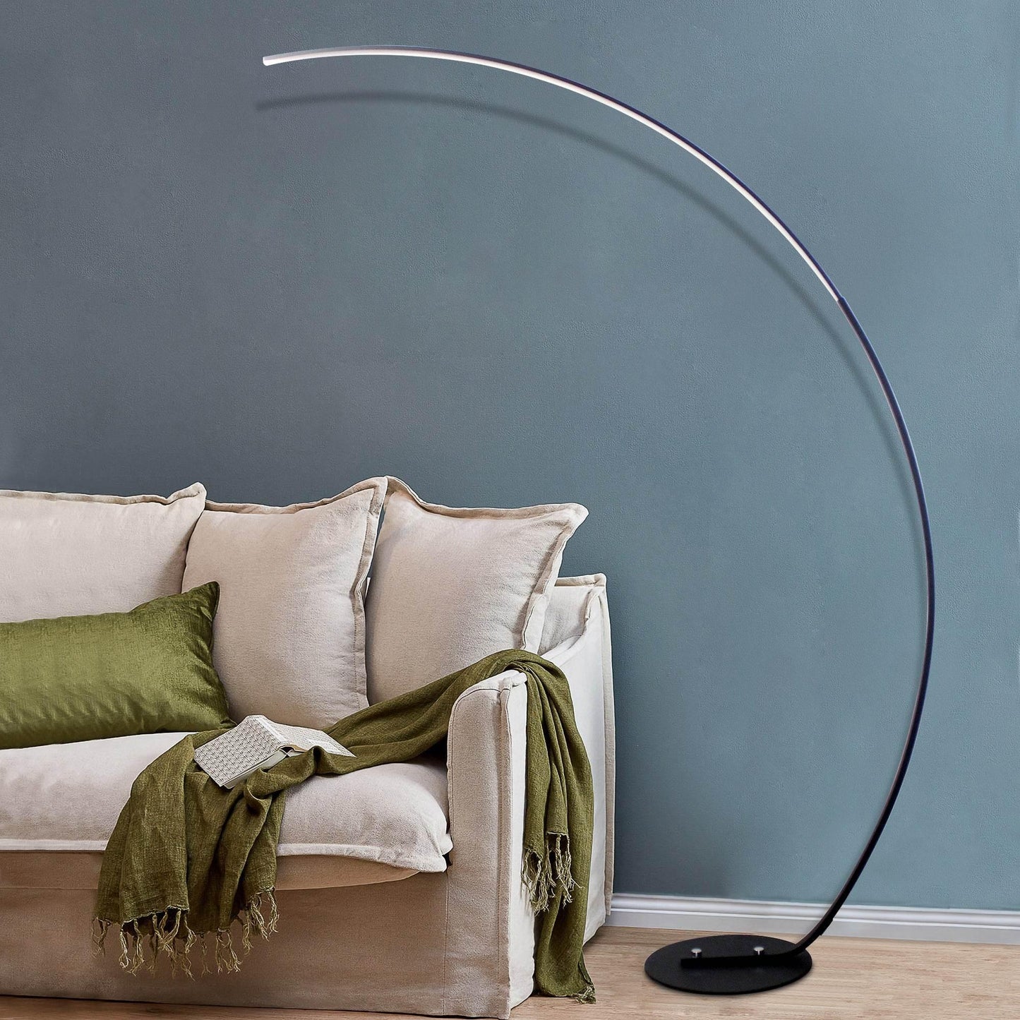 Sangria Apricot modern curve floor lamp with sleek black arc design next to beige sofa with green cushions