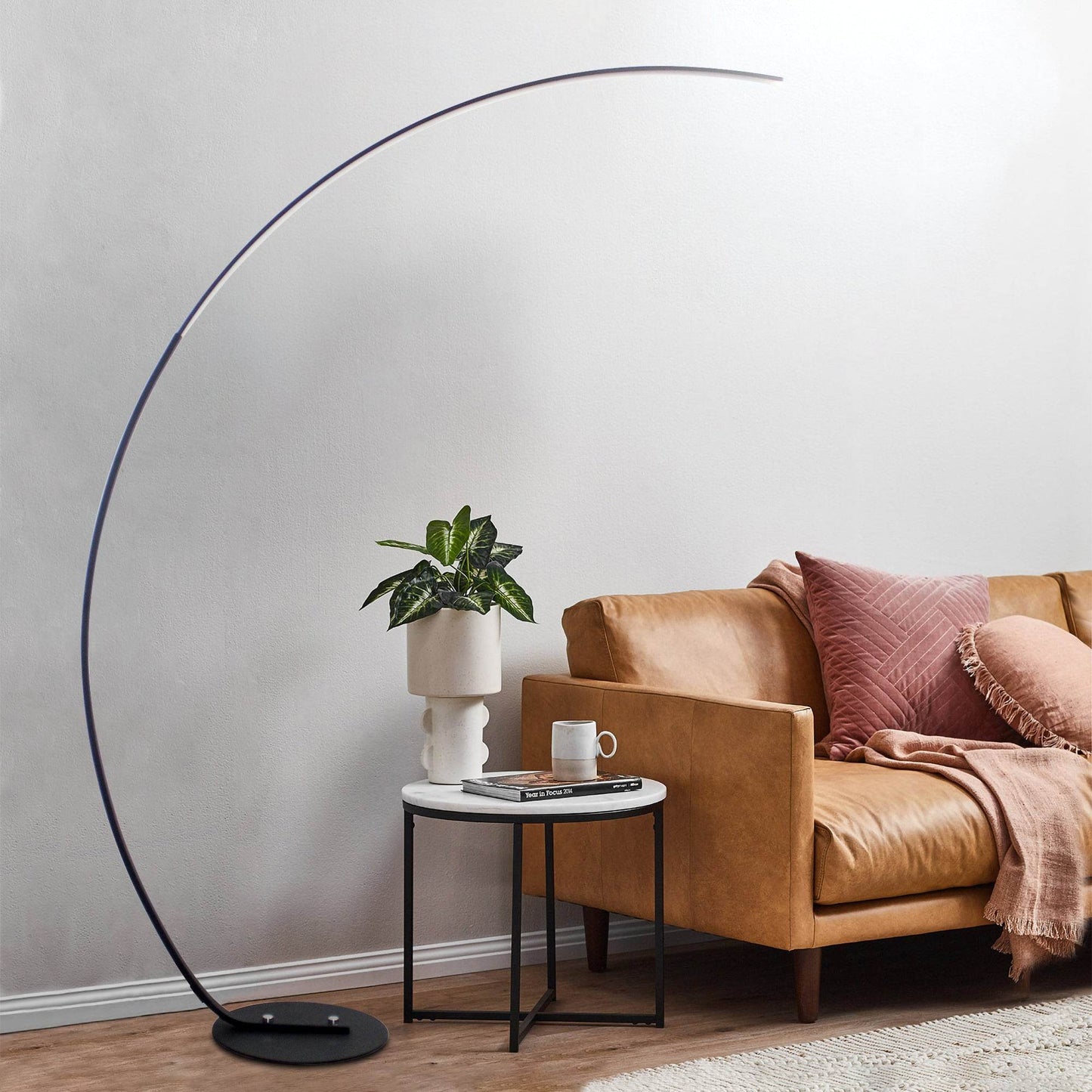 Sangria Apricot modern curve floor lamp next to tan sofa and side table with plant in contemporary living room