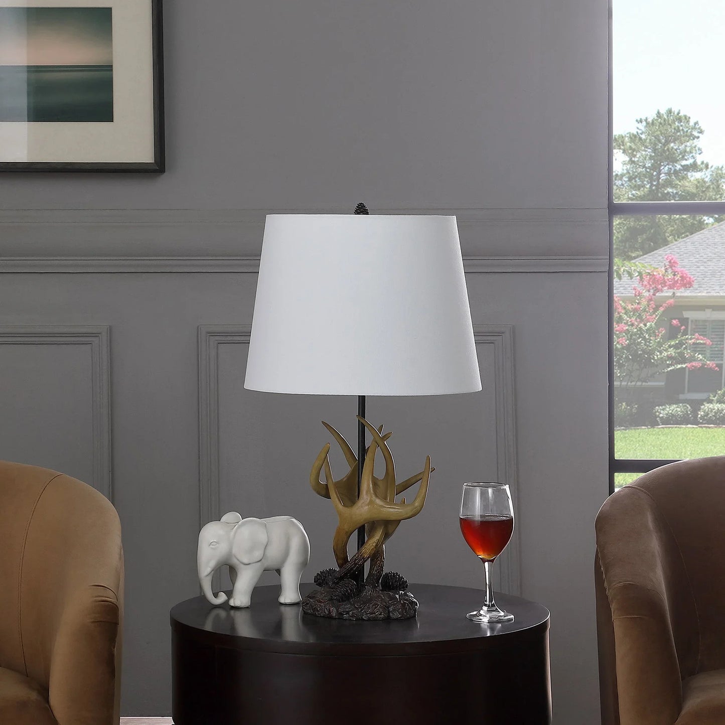 Natural antlers lamp with white shade on a round black table between two brown chairs