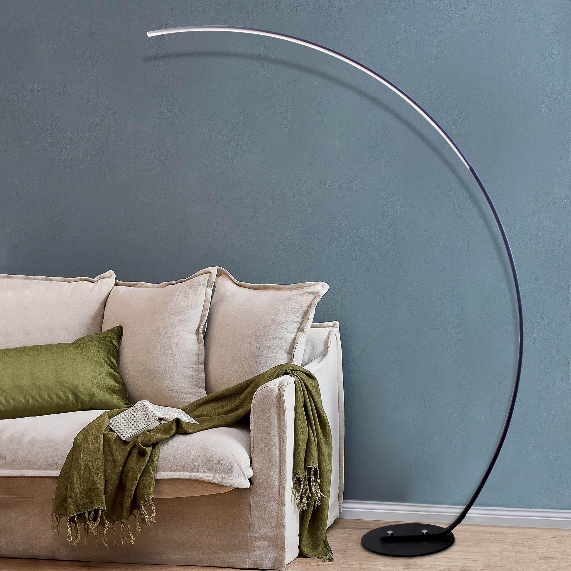 Sangria Apricot modern curve floor lamp with sleek black arc design next to beige sofa with green cushions
